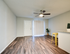 Bright living space with elegant wood flooring, modern ceiling fan, and open access to kitchen with sleek countertops and a stylish yellow stool.