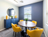 Bright, modern dining area with vibrant yellow chairs, a circular wooden table, and a stylish blue cabinet with a mirror.