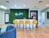 Vibrant reception area featuring a modern neon sign, lush green wall, and stylish yellow barstools at The Iris.