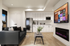 Modern living room with cozy black sofa, sleek white kitchen cabinets, and vibrant electric fireplace under large smart TV.