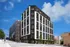 Modern urban apartment building with sleek black and white architecture, situated on a vibrant city street under a clear blue sky.