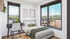 Bright, modern bedroom with large windows offering stunning city and forest views, featuring a cozy bed, sleek desk, and stylish decor.