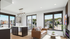 Sleek modern living room filled with natural light, showcasing large windows with scenic views, a cozy leather sofa, stylish kitchen island, and ambient fireplace.
