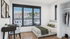 Modern bedroom with a large window offering stunning city views, featuring a cozy bed and a neat workspace.