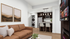 Modern living space with a luxurious brown leather sofa, chic kitchen island with seating, and stylish wall art. Features an open floor plan, mounted TV, and in-unit washer-dryer.