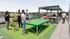 Vibrant rooftop terrace featuring a community game area with ping pong and giant Jenga, surrounded by socializing people enjoying the outdoor barbecue area.