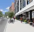 Vibrant cityscape featuring a modern apartment building with stylish outdoor seating and bike-friendly amenities on a sunny street.