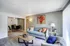 Inviting living room with modern decor, featuring a cozy blue sofa adorned with vibrant cushions, a chic wooden coffee table, stylish artwork, and an elegant dining area in the background.