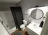 Modern bathroom with sleek design, featuring white vanity, round mirror, and elegant black shower curtain.