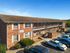 Charming brick apartment building with ample parking and well-maintained landscaping under a clear blue sky.