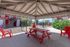 Charming outdoor communal area with vibrant red picnic seating under a cozy gazebo, overlooking a fenced pool and lush greenery.