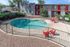 Inviting apartment building with a refreshing oval pool, surrounded by lush greenery and vibrant red lounge chairs for relaxation.