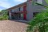 Charming apartment exterior with vibrant red doors and lush greenery, featuring modern balcony design and a serene stone courtyard.