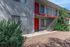 Charming apartment complex with vibrant red doors, lush greenery, and an inviting stairway under a clear blue sky.