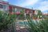 Charming apartment complex with a refreshing pool, vibrant red accents, and lush greenery under a bright blue sky.