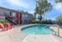 Bright apartment complex with inviting pool and vibrant red chairs set against a clear blue sky, offering a refreshing outdoor escape.