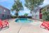 Inviting outdoor pool area with vibrant red chairs, surrounded by lush greenery and modern apartments.