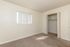 Bright and inviting bedroom with soft carpet flooring, large closet, and natural light streaming through a window with vertical blinds.