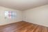 Bright empty room with elegant wood flooring and abundant natural light from a large window, perfect for personalizing your living space.