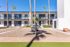 Bright and inviting apartment complex with modern architecture, featuring a stylish courtyard, lush palm trees, and an outdoor grill under a clear blue sky.
