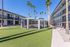 Contemporary apartment complex with a lush green courtyard, inviting swimming pool, and towering palm trees under a clear blue sky.