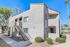 Modern apartment building exterior with vibrant landscaping and elegant architecture, showcasing a charming balcony and staircase under a clear blue sky.