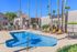 Inviting apartment complex pool area with vibrant lounge chairs, palm trees, and relaxing umbrellas under a clear blue sky.
