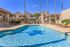 Inviting outdoor pool area with sun loungers and vibrant landscaping, surrounded by charming Mediterranean-style apartment buildings.