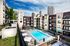 Luxurious urban apartment complex featuring a sparkling pool, modern architecture, and lush landscaping with city skyline views.