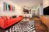 Contemporary apartment interior with a vibrant red sofa, artful decor, a stylish kitchen, and warm wood flooring.