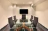 Modern conference room with a sleek glass table, black leather chairs, and wall-mounted TV.