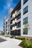 Modern apartment exterior with sleek balconies, lush landscaping, and ample parking space under a vibrant blue sky.