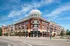 Modern urban apartment complex with stylish brick facade, featuring retail shops on the ground floor and spacious balconies, set against a clear blue sky.