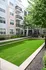 Charming apartment exterior with modern balconies overlooking a beautifully landscaped courtyard with lush green grass and mature trees.