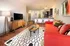 Chic living room with vibrant red sofa, patterned cushions, modern wooden furniture, and open-concept kitchen with sleek bar stools.