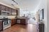 Modern open-concept apartment showcasing a stylish kitchen with dark wooden cabinets, sleek countertops, and stainless steel appliances opening to a bright living area.