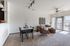 Bright and spacious living area featuring a cozy sectional, plush armchair, and elegant dining table, enhanced by natural light from large windows.
