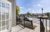 Charming apartment entrance featuring a sunny porch with modern railing, overlooking a well-maintained, tree-lined street and spacious parking area.