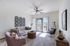 Bright and inviting living room with modern decor, featuring a comfortable beige sofa, stylish pink armchair, and elegant wicker coffee table. Large windows let in natural light, creating a warm and welcoming atmosphere.