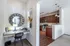 Elegant apartment corner featuring a stylish workspace with a chic mirror, adjacent to a modern kitchen with dark wood cabinets and stainless steel appliances.