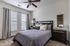 Inviting bedroom with elegant decor, featuring a comfortable bed adorned with cozy pillows, natural light from large windows, and a stylish ceiling fan.