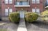 Inviting brick apartment entrance with lush shrubs and a charming balcony, offering a warm welcome.