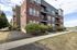 Charming brick apartment building featuring modern balconies, lush green landscaping, and a serene walkway.