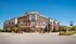 Elegant brick apartment complex with modern design, featuring spacious balconies and vibrant landscaping under a clear blue sky.