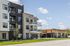 Modern apartment building with sleek balconies, large windows, and lush landscaping under a bright blue sky.