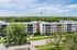 Modern apartment complex surrounded by lush greenery and bright blue skies, featuring contemporary architectural design.
