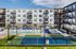 Modern apartment complex featuring a sparkling outdoor pool, sun loungers, and a tennis court, set against a backdrop of stylish multi-story buildings with private balconies.