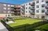 Modern apartment building with spacious balconies and a vibrant courtyard featuring lush green spaces and seating areas.
