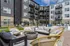 Chic apartment complex with modern outdoor seating area, vibrant wicker chairs, and cozy fire pit under a sunny sky.