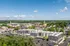 Vibrant aerial view of a modern apartment complex nestled in a charming city center, surrounded by lush greenery and blue skies.